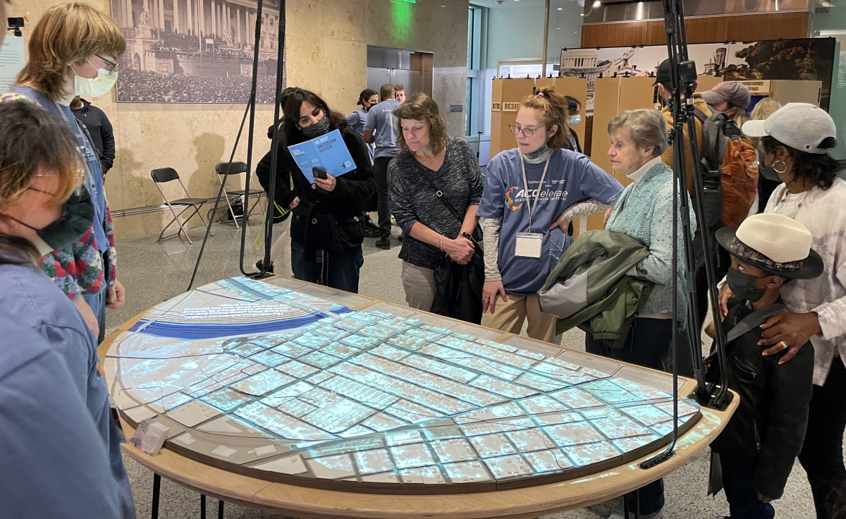 A group of people stand around a table on which is projected a map of Selma, AL