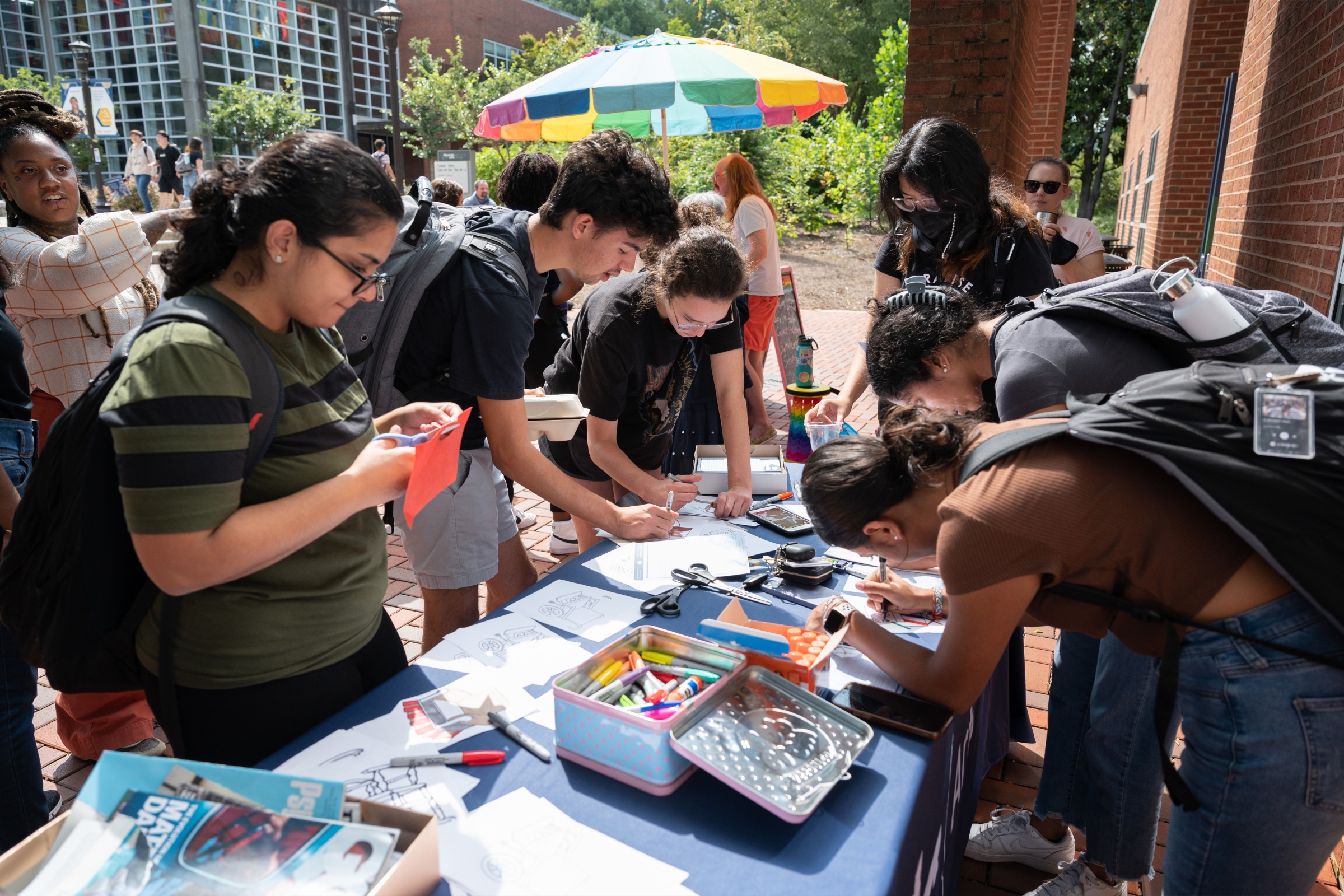 People crowd around a table filled with art supplies