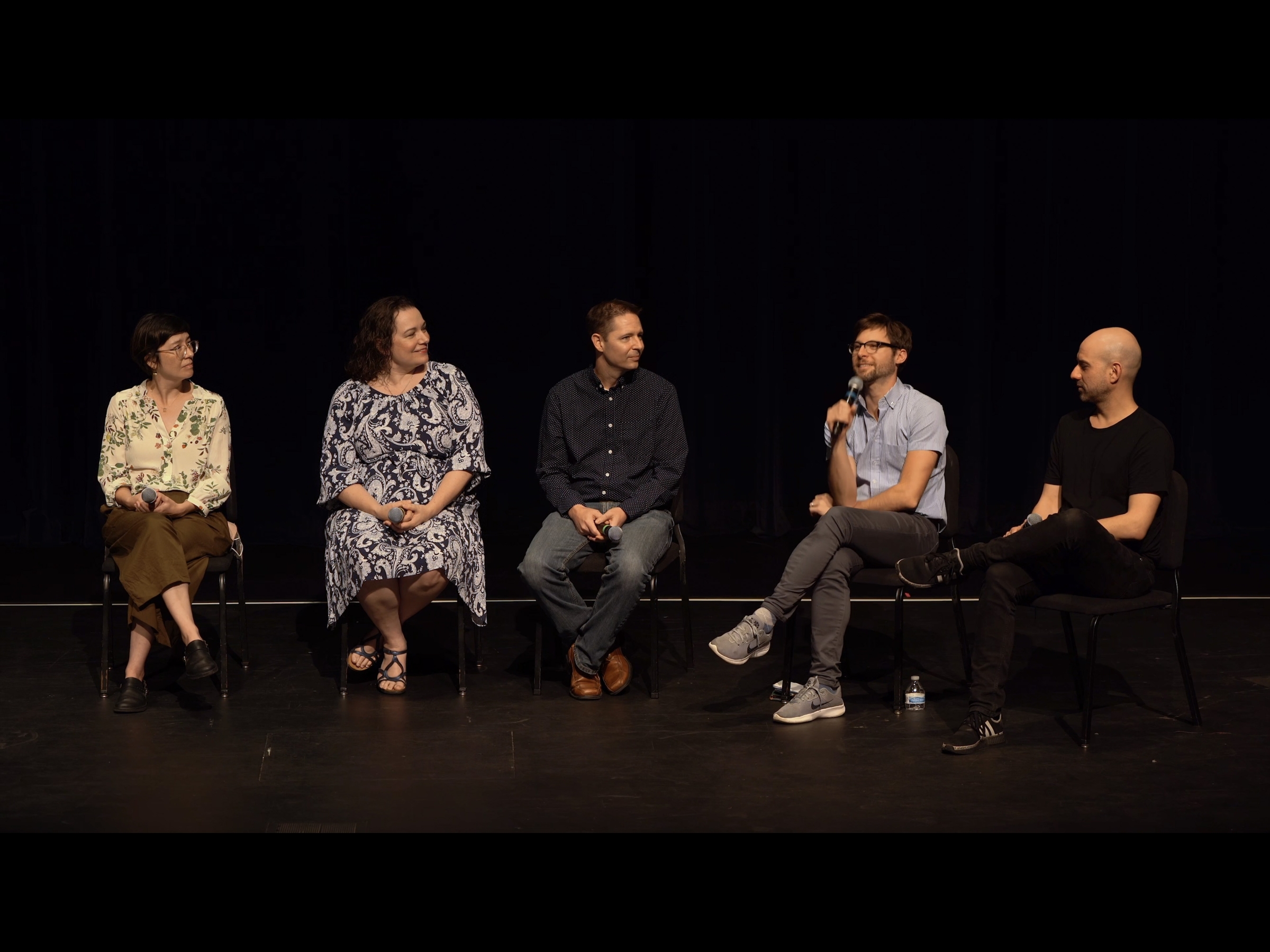 Five casually dressed people sit in chairs in a row for a panel discussion