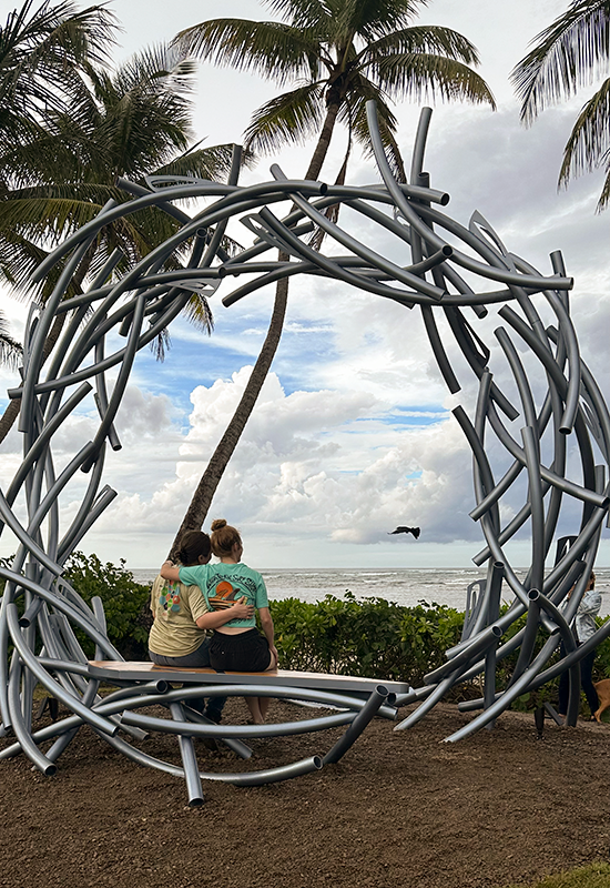 Danielle and Elizabeth sitting on the sculpture’s bench with heir back to the camera.