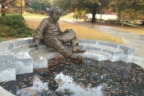 Bronze figure of Albert Einstein, reclining on marble steps with papers in his lap, reflecting on the map of the sky engraved in the ground below him.