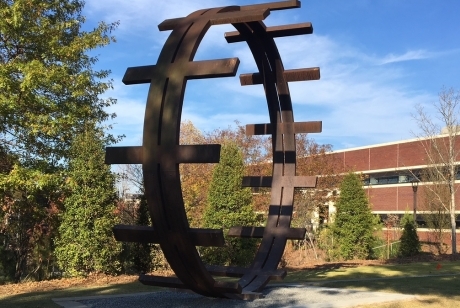 Circular band of steel, one point resting on the ground, with bars placed perpendicular to the circle almost as if it creates a ladder