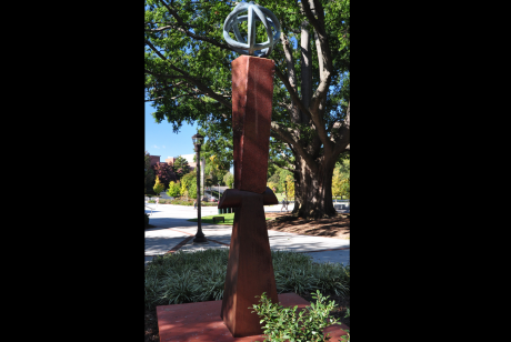 A four-sided vertical made of granite and wood, cinched in the middle with an orb on top