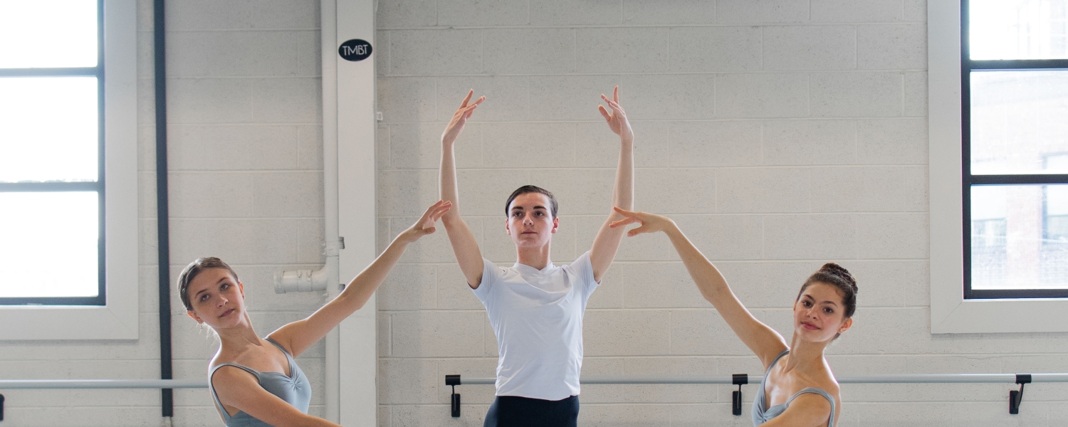 Four dancers are posed as a classical quartet. The three women wear pale blue leotards with gauzy white skirts. The man wears a white T shirt and black tights.