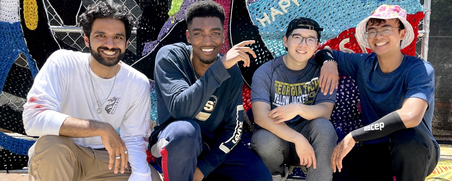 Four young men from the Tech student organization TekStyles, crouch in front of the mural.
