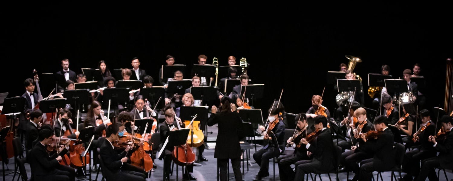 Two dozen musicians in formal clothes seated while playing instruments