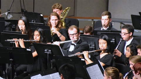 A dozen musicians in formal wear play wind instruments