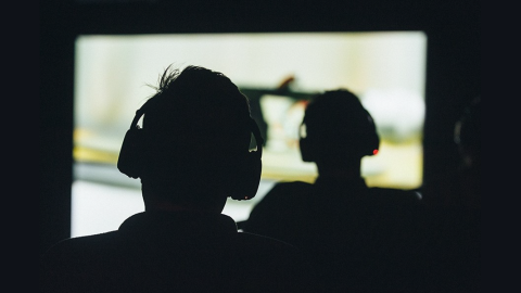 The silhouette of two people seen from the back, each wearing headphones and looking at a projected image on a movie screen. / Photo by Catalina Kulczar