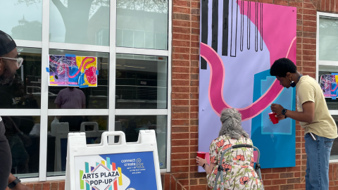 People stand outside at the wall the Ferst Center for the Arts, painting on the canvasses installed between two windows.