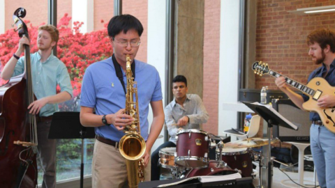 Three male musicians each playing the bass, saxophone, electric guitar, and drums.