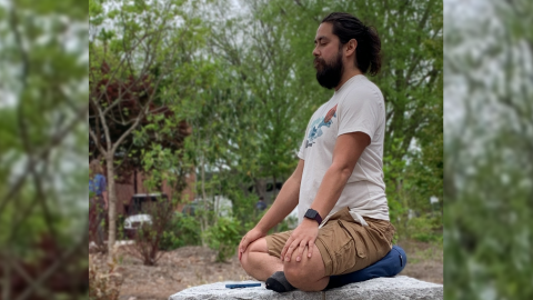 A man sits on a stone ledge, his legs crossed in a yoga position.