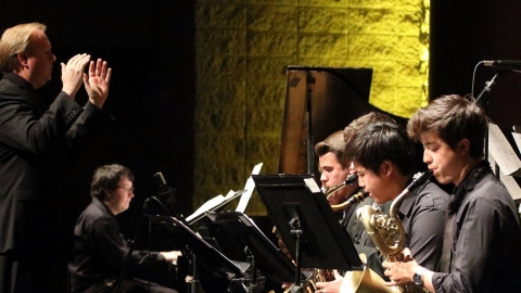 Photo of musicians playing instruments while conductor stands in front