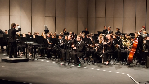 Group of musicians on stage playing various instruments with director standing in front 