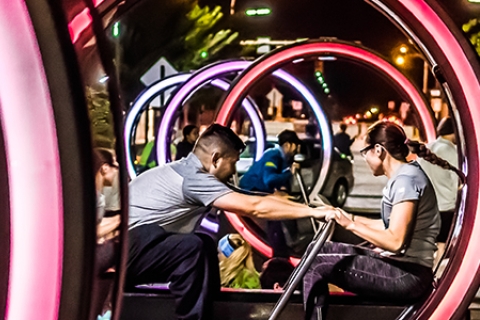 Two people are sitting facing each other inside a large circular frame with their hands on a push bar between them