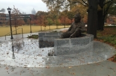 Bronze figure of Albert Einstein, reclining on marble steps with papers in his lap, reflecting on the map of the sky engraved in the ground below him.