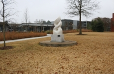 Smooth white marble, only lightly veined, sculpted as an abstract rendering of the olympic flame. The sculpture sits on asquare marble pedestal on a round cement base, placed on a grassy, gently sloping hill.
