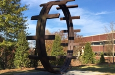 Circular band of steel, one point resting on the ground, with bars placed perpendicular to the circle almost as if it creates a ladder