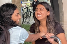 Two young women with broad smiles sit facing eachother with the pushbar of a Loop between them.