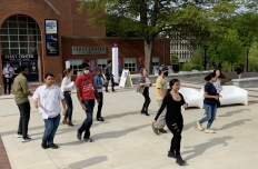 A woman dressed in all black stands in front of a group of students to teach them how to dance. GT Salsa student organization.