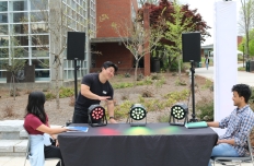 Two people sit at opposite ends of a table, their hands in front of them on sensors and colorful lights on the table between them. Empathy Between Two by grad student Tim Min.