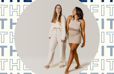 Two barefoot women wearing beige clothing walk hand in hand