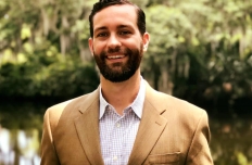 a man seen from the chest up, wearing a tan blazer