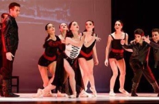 A ballet company on stage. A scrum of dancers surround the main character, a woman in red