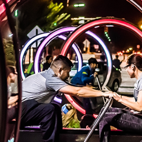 Two people are sitting facing each other inside a large circular frame with their hands on a push bar between them